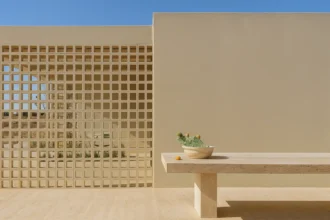 Imagem de uma fachada moderna com uma parede de blocos de vidro e um banco de concreto, sob um céu azul claro. O foco está na arquitetura minimalista e na combinação de elementos de design clean.
