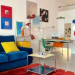 Ambiente vibrante e moderno com sofá azul, tapete vermelho e arte colorida, refletindo o estilo Funhaus de decoração alegre e contemporânea.