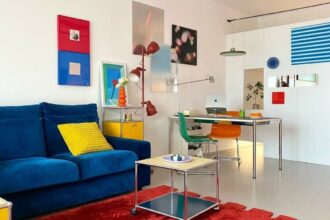 Ambiente vibrante e moderno com sofá azul, tapete vermelho e arte colorida, refletindo o estilo Funhaus de decoração alegre e contemporânea.
