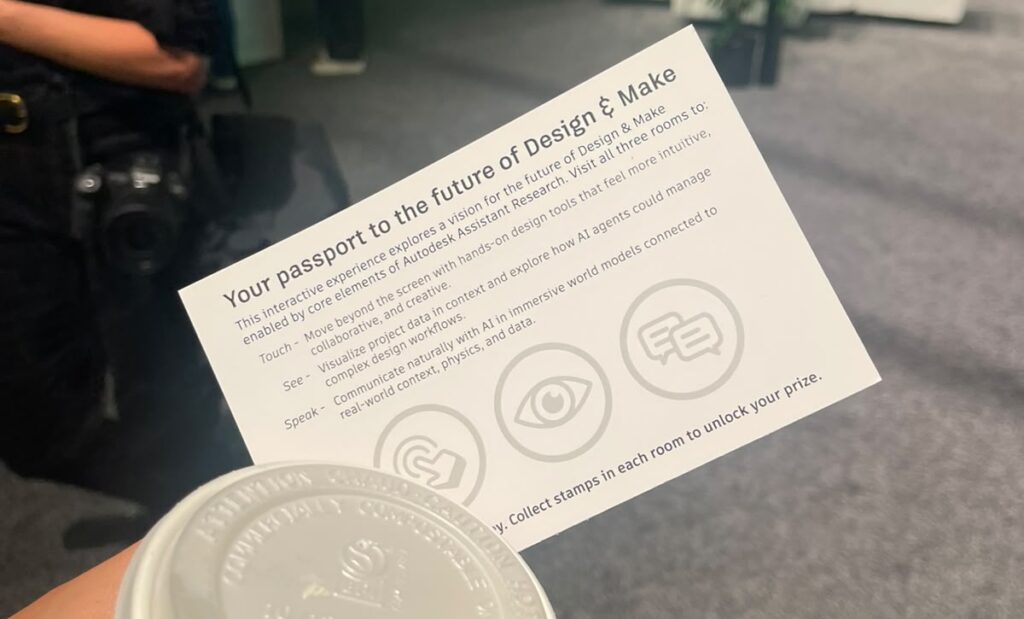 Participante em um evento como a Autodesk University 2026 segurando um copo de café e um folheto 'Your passport to the future of Design & Make', que explora o futuro do design e da manufatura com a pesquisa Autodesk Assistant.