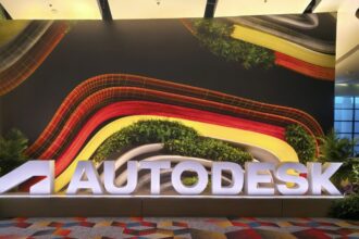 Letreiro luminoso AUTODESK em destaque na entrada de um evento, com um fundo de parede vibrante de design orgânico e elementos verdes, capturando o ambiente da Autodesk University 2026.